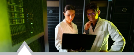 male and female engineers wearing aprons using laptop while inspecting in server room